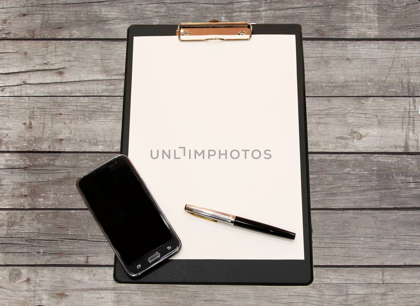 A white sheet of paper with a pen and smartphone on a wooden table made of grey Board