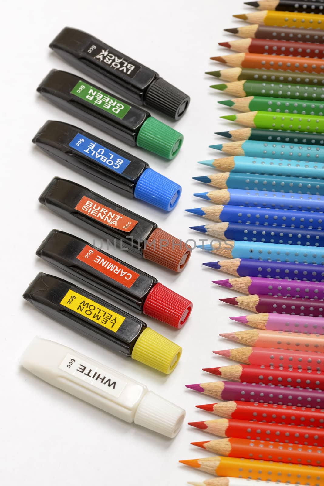 Bundle of colored pencils and tubes of paint on the colorful background