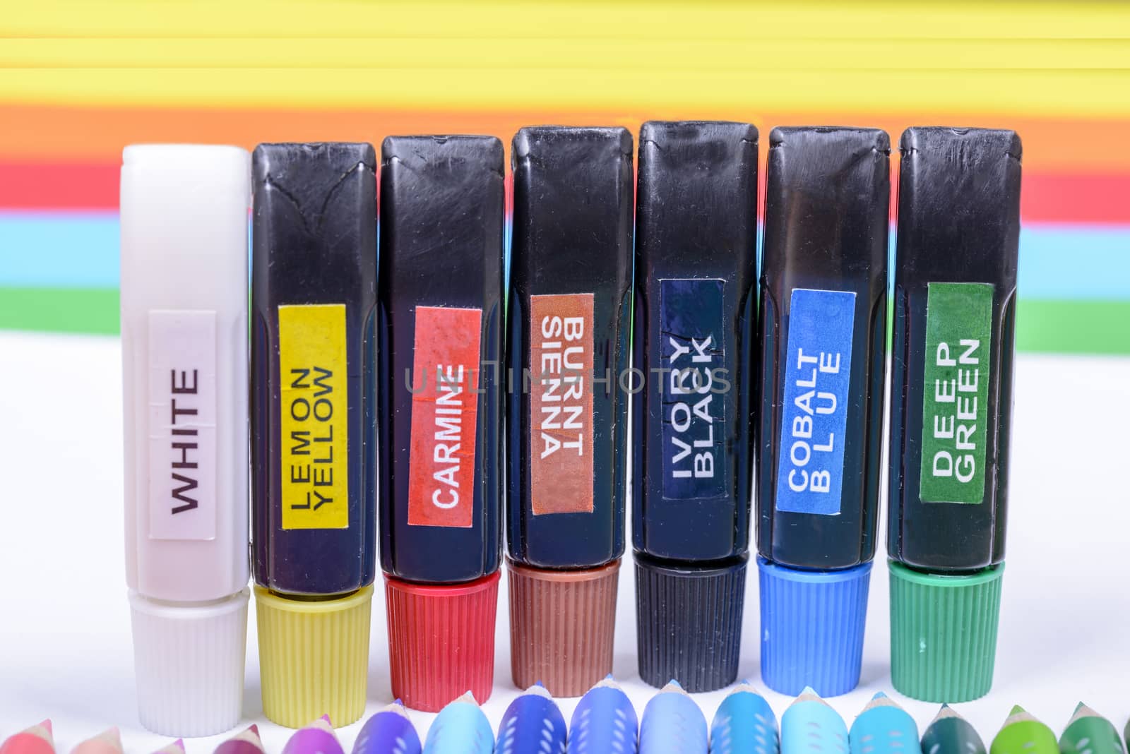 Bundle of colored pencils and tubes of paint on the colorful background