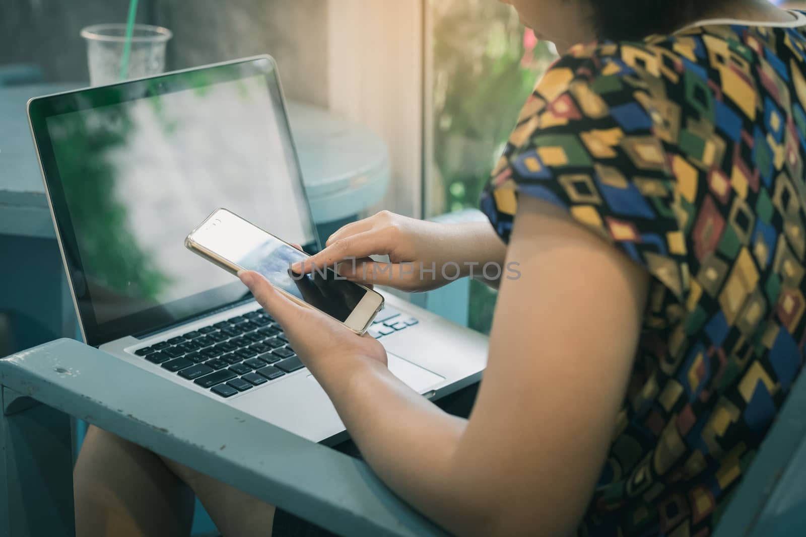 Asian woman using smartphone at home while working with laptop computer. Online business and wireless working from anywhere concept with vintage filter effect