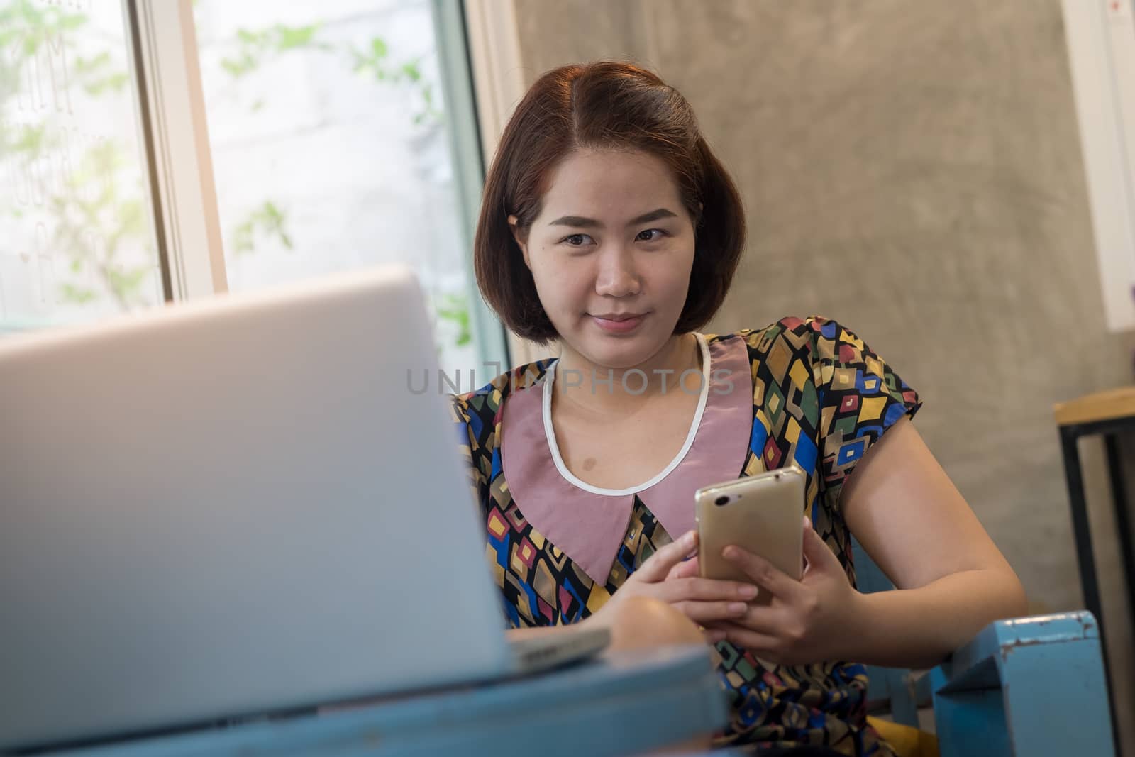 Asian woman using smartphone at home while working with laptop computer. Online business and wireless working from anywhere concept