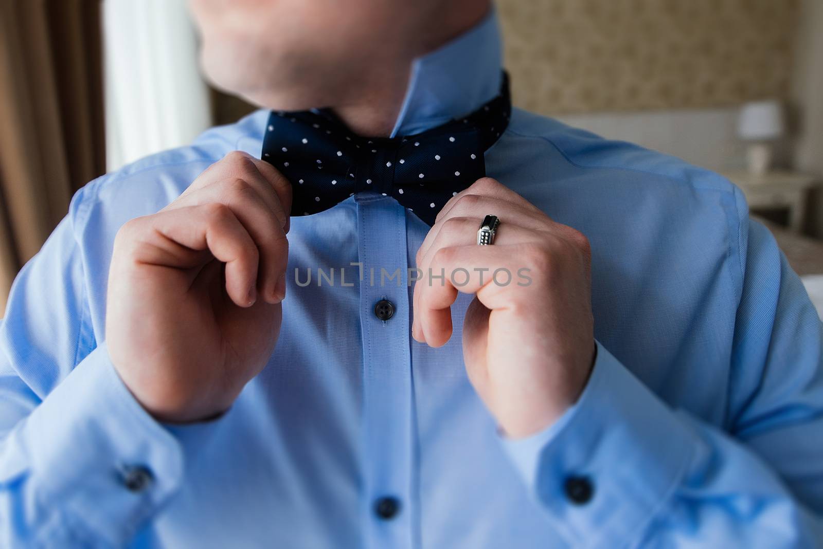The groom in a blue shirt holding a bow tie in his hands