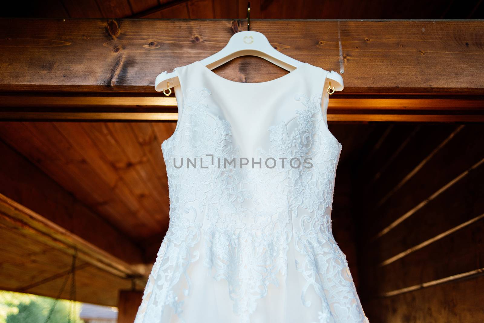 A beautiful cream wedding dress hanging on the wall near the wooden house