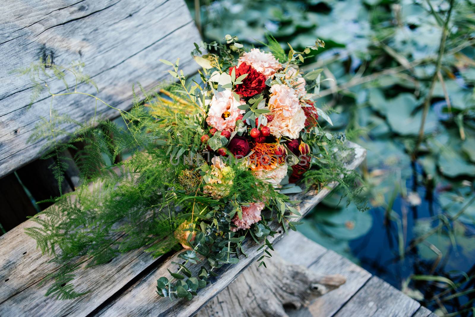 Lush wedding bouquet on a gray wooden bench near the water with water lily