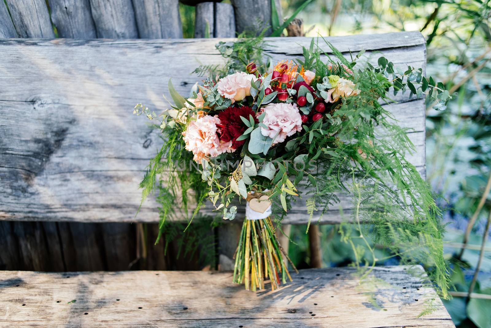 Lush wedding bouquet on a gray wooden bench near the water with water lily