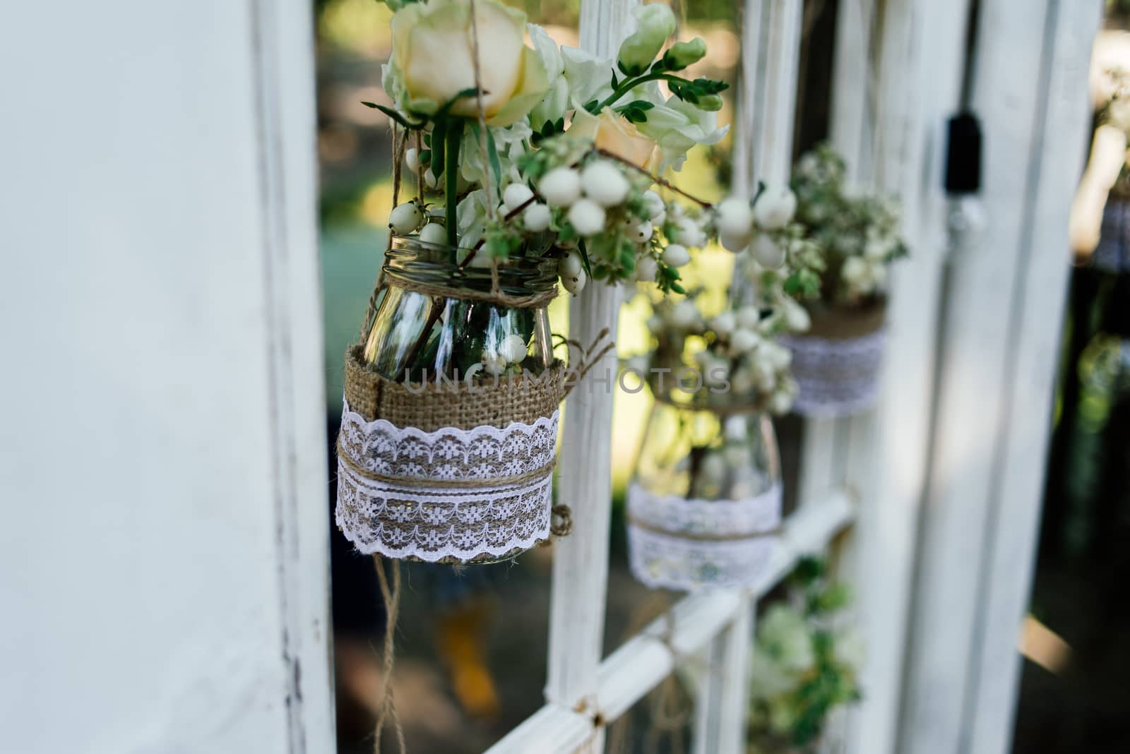 Little wedding floral decorations in rustic style hang in jars decorated with sacking and lace