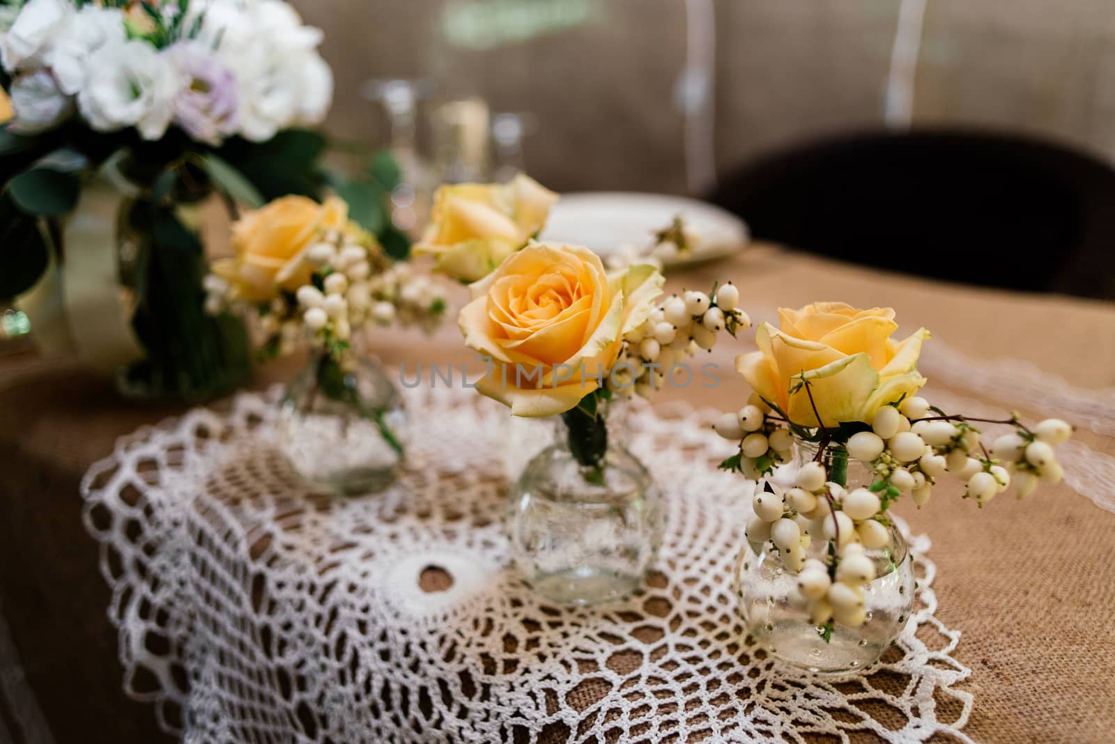 Little wedding floral decorations of yellow roses are in vases on dinner table