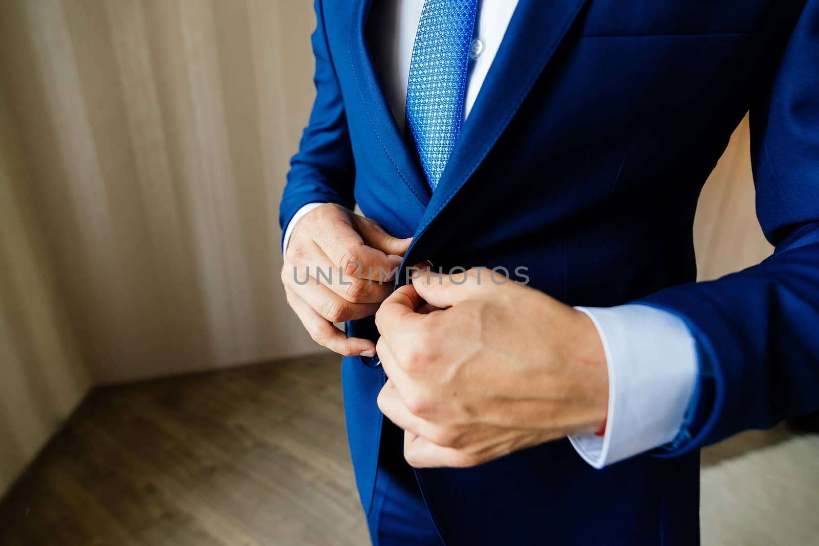 The groom fastens the button on his jacket