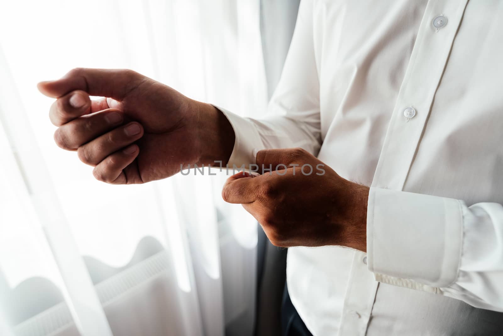 A man in a white shirt buttoning a button on a shirt cuff by d_duda