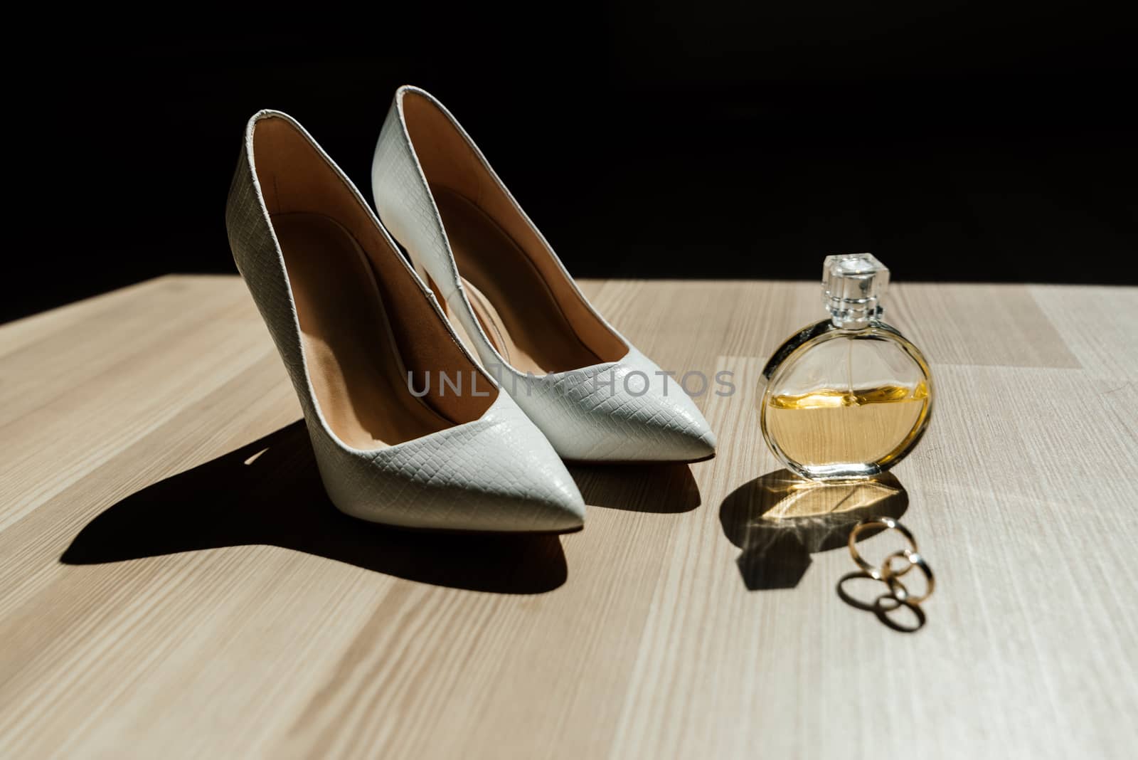 Bride's shoes, perfume and wedding rings are on the table