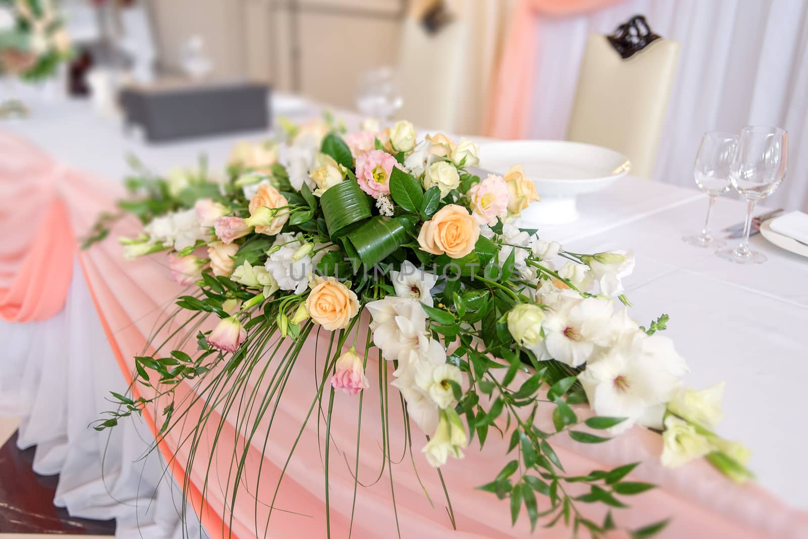 Lush wedding floral decorations on dinner table covered with peach cloth. Table for the newlyweds.