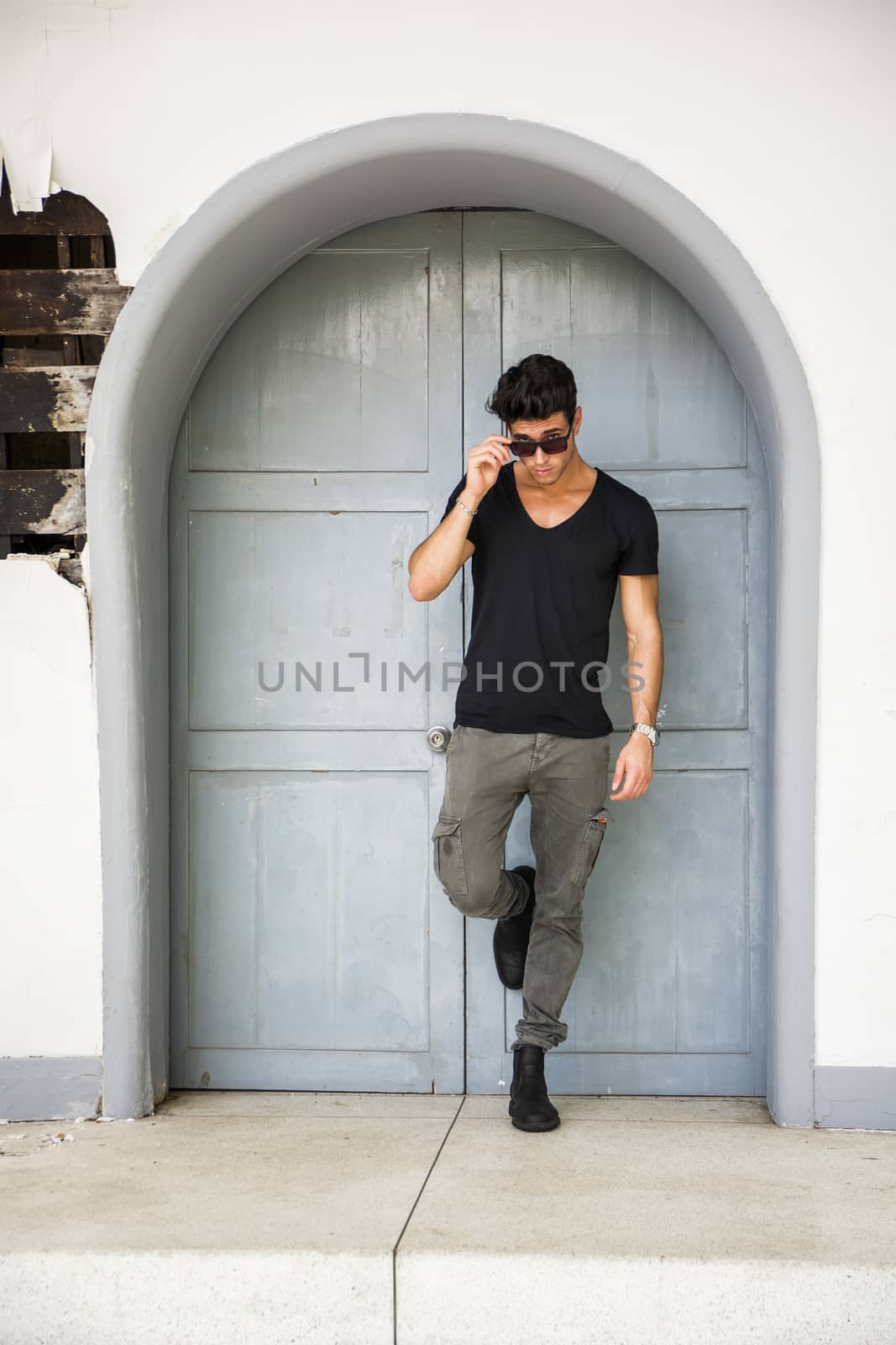 Handsome young man outdoors in front of old house's wood entrance door, looking away to a side