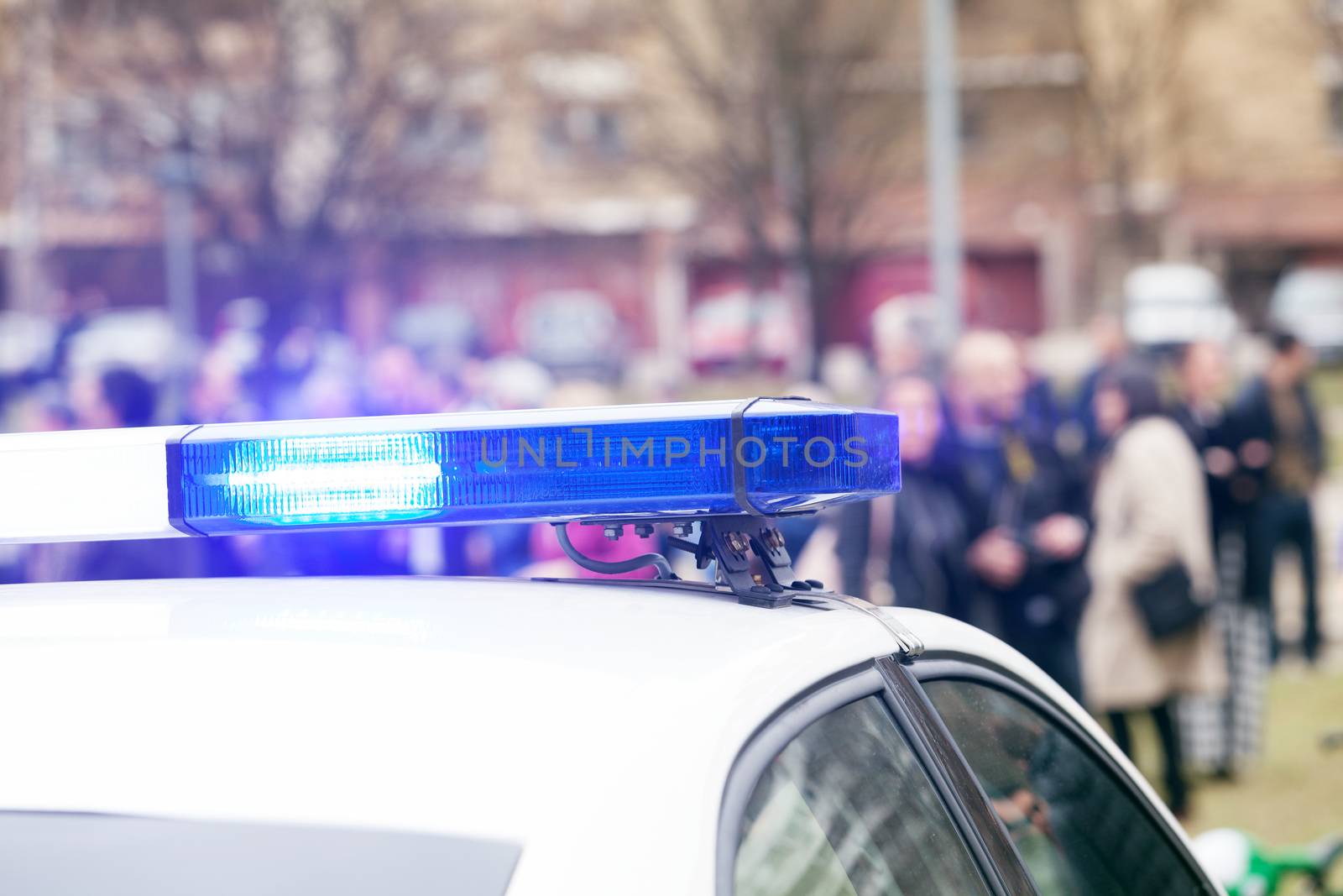 Police car flashing lights in focus, blurred crowd in background by wellphoto