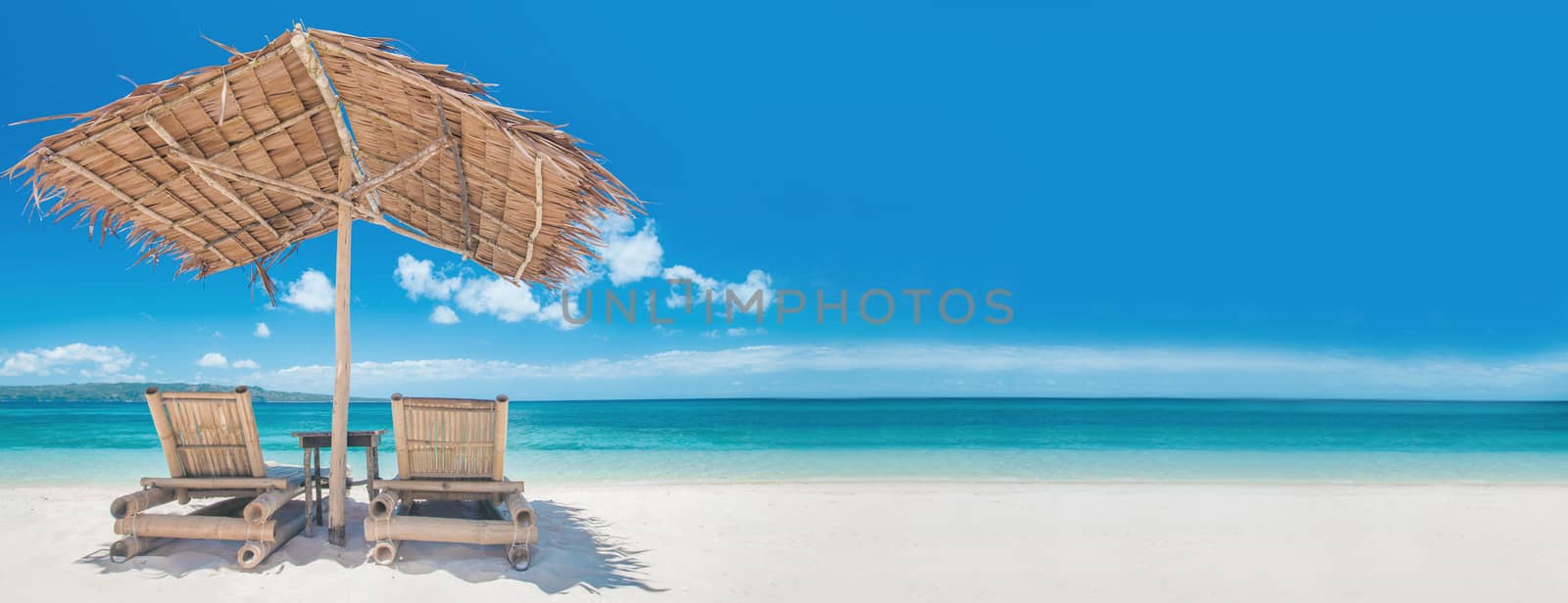 Two bamboo chairs under straw umbrella on tropical beach