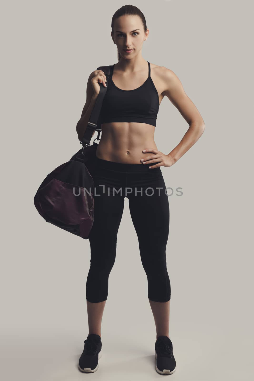 Portrait of sporty young woman posing with a gym bag,  against a gray background