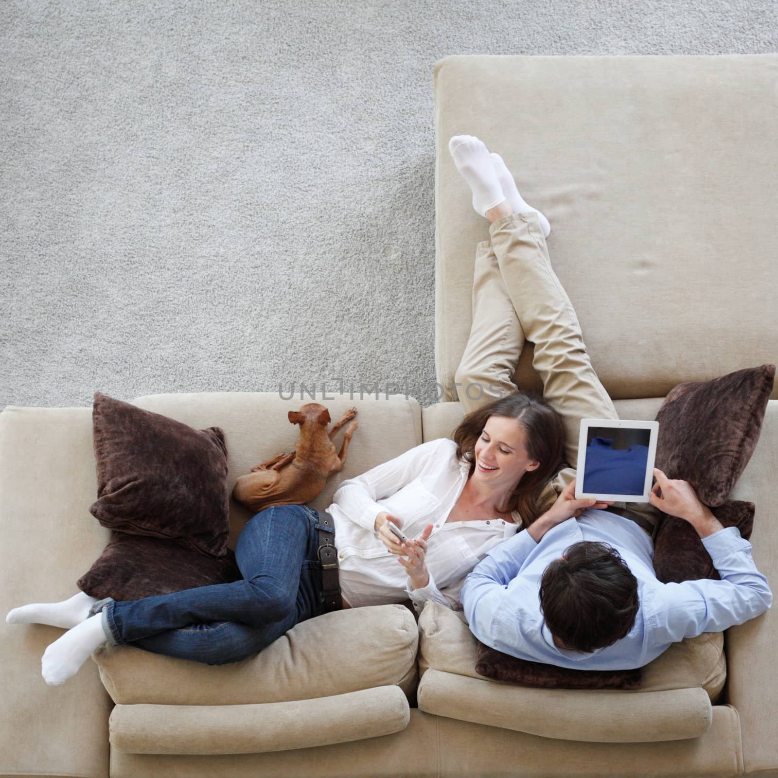 Couple using digital tablet at home sitting on sofa, top view