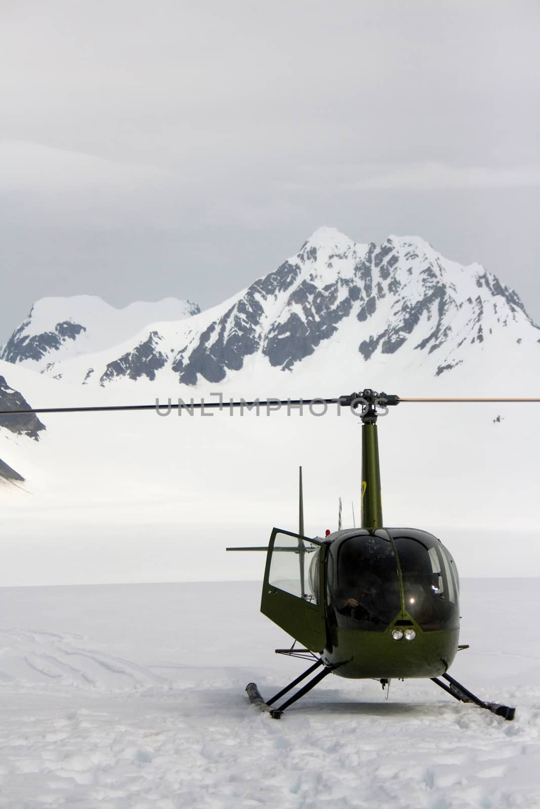 A small green helicopter lands on top of a snow-covered glacier near Seward, Alaska. 