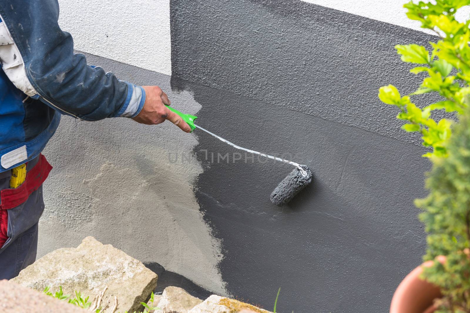 Close-up, arm of a house painter with paint roller in hand painting a house wall with gray paint.
