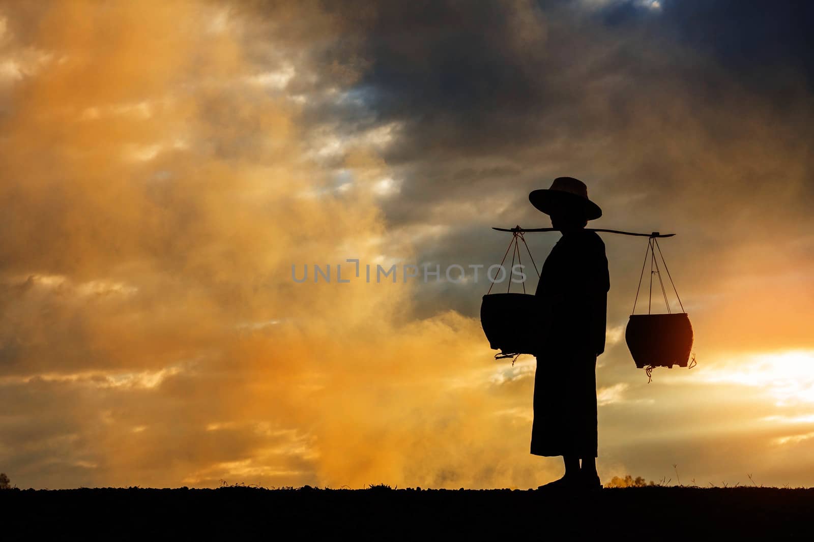 Female farmer walking of basket on fields at sunset.