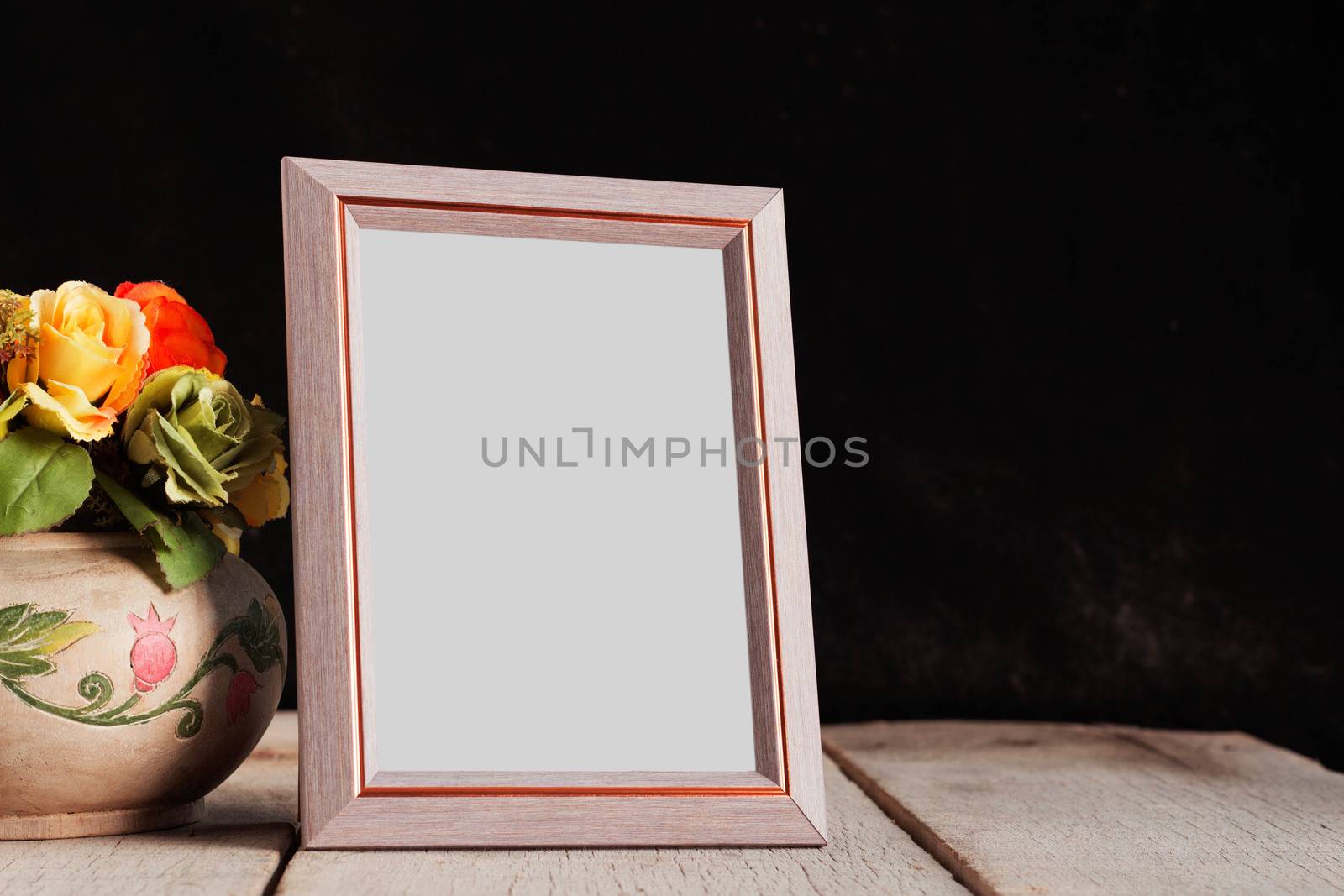 Old photo frame with flower vase on wooden table.