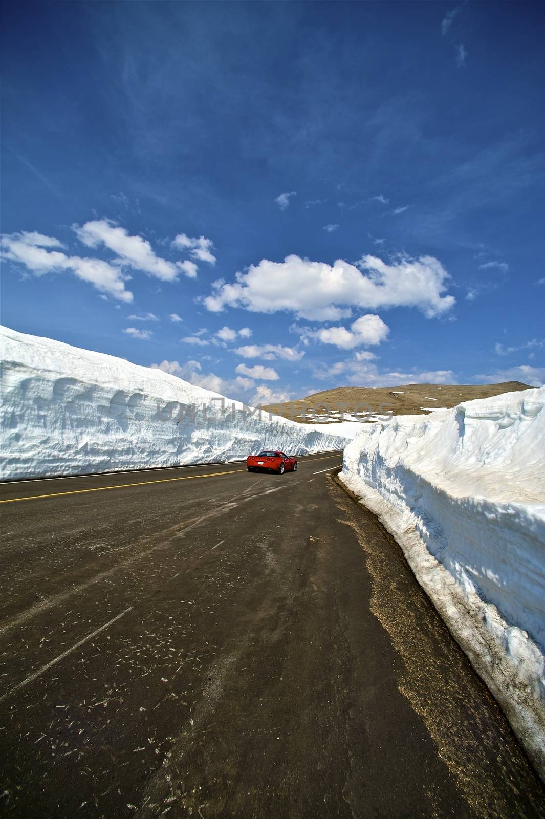 Early Summer Mountains Road Ride. Massive Snowfields Both Sided of the Road and Red Sport Car. Rocky Mountains National Park, Colorado USA. Vertical Photo