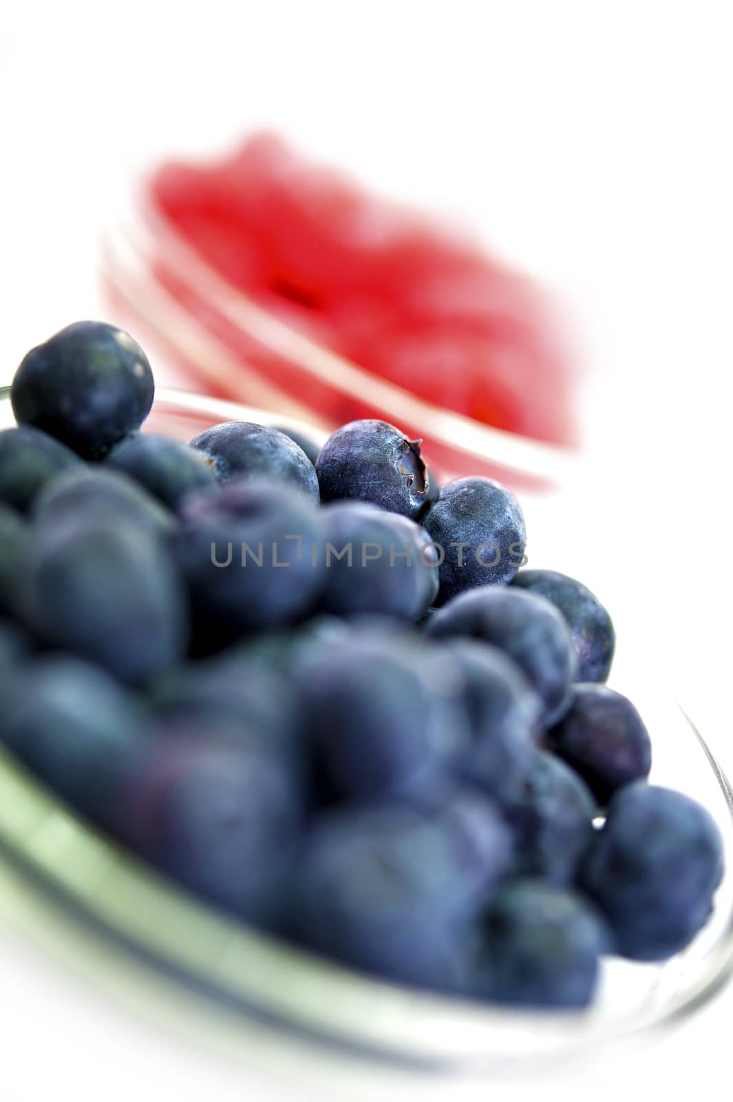 Fresh Raw Blueberries in Glass Bowl. Out of Focus Raspberries in Background