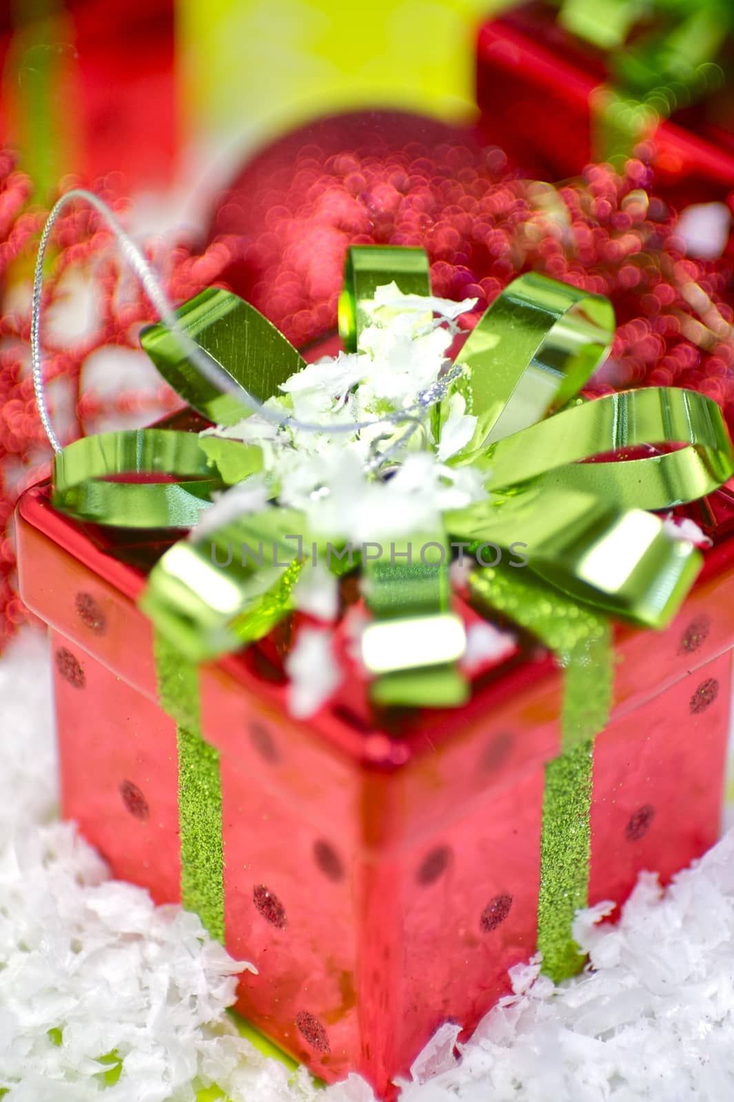 Christmas Gift. Red Christmas Present Box with Green Glossy Bow. Some Fake Snow and Holiday Ornaments. Beautiful Christmas Theme.