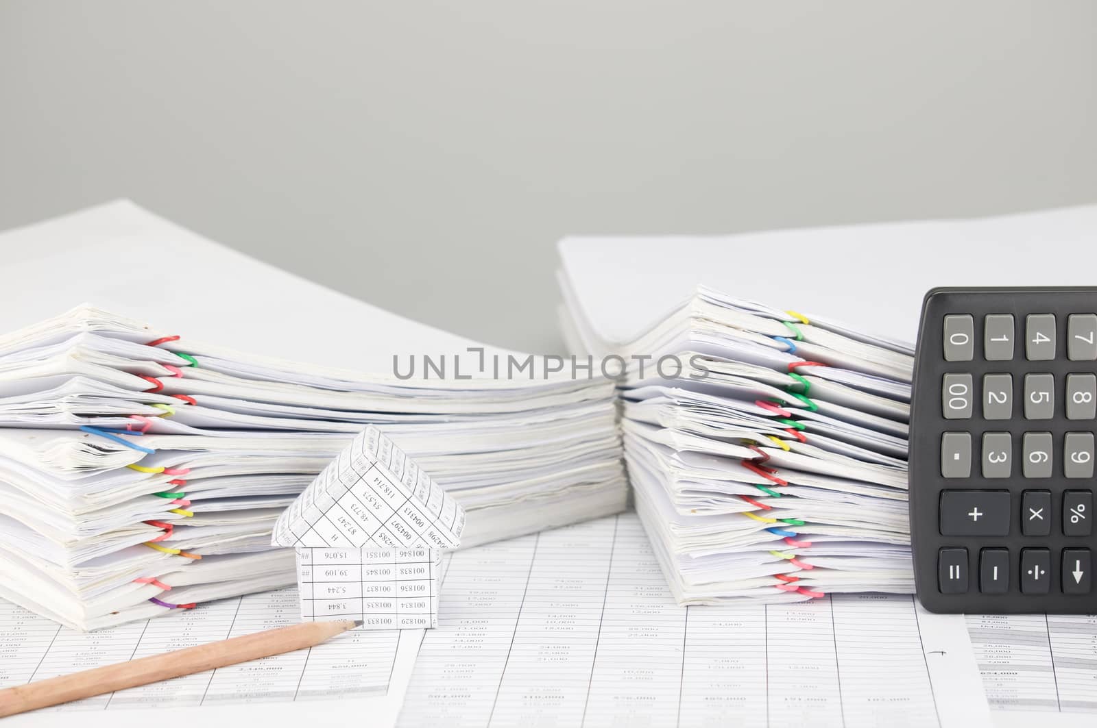 House and pencil on finance account have pile overload document of report and receipt with colorful paperclip and calculator place vertical as background.