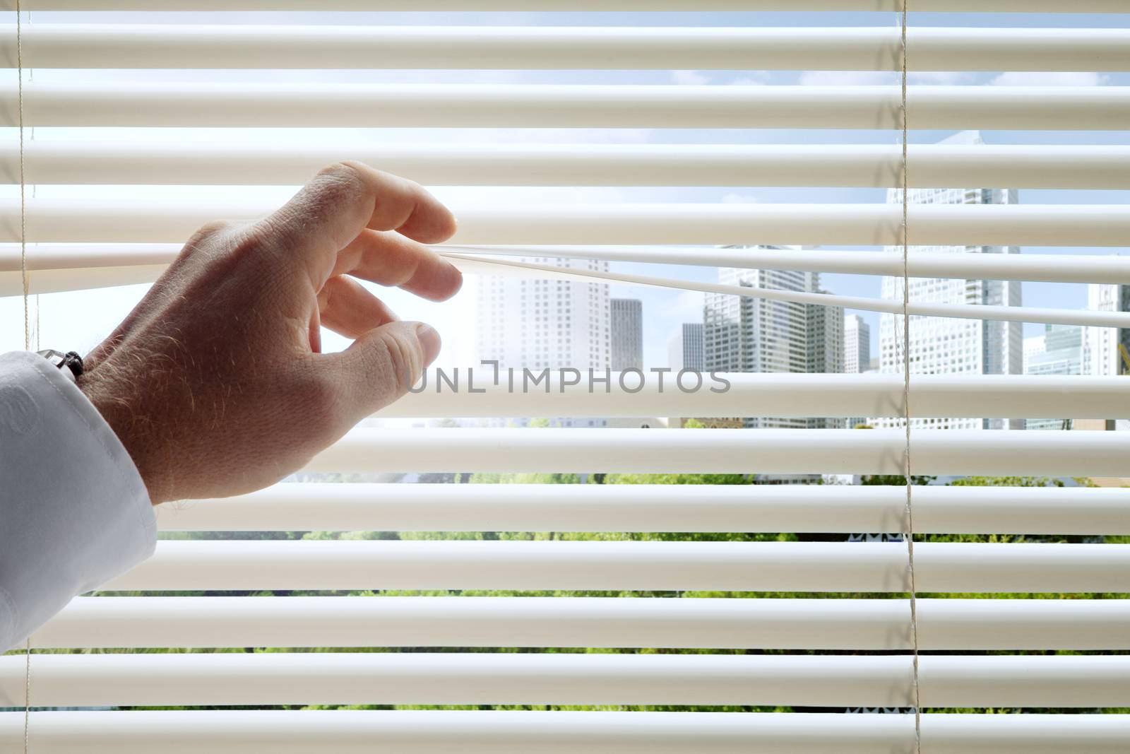 close up view of man's head spreading blinds and sunny city  background