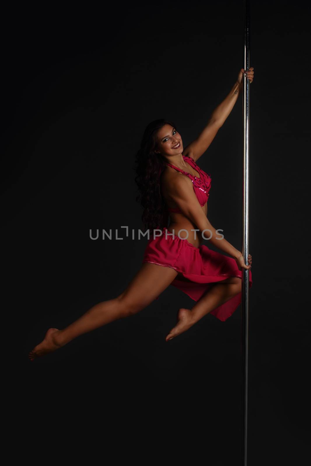 Beautiful woman performing pole dance, studio shot on black background