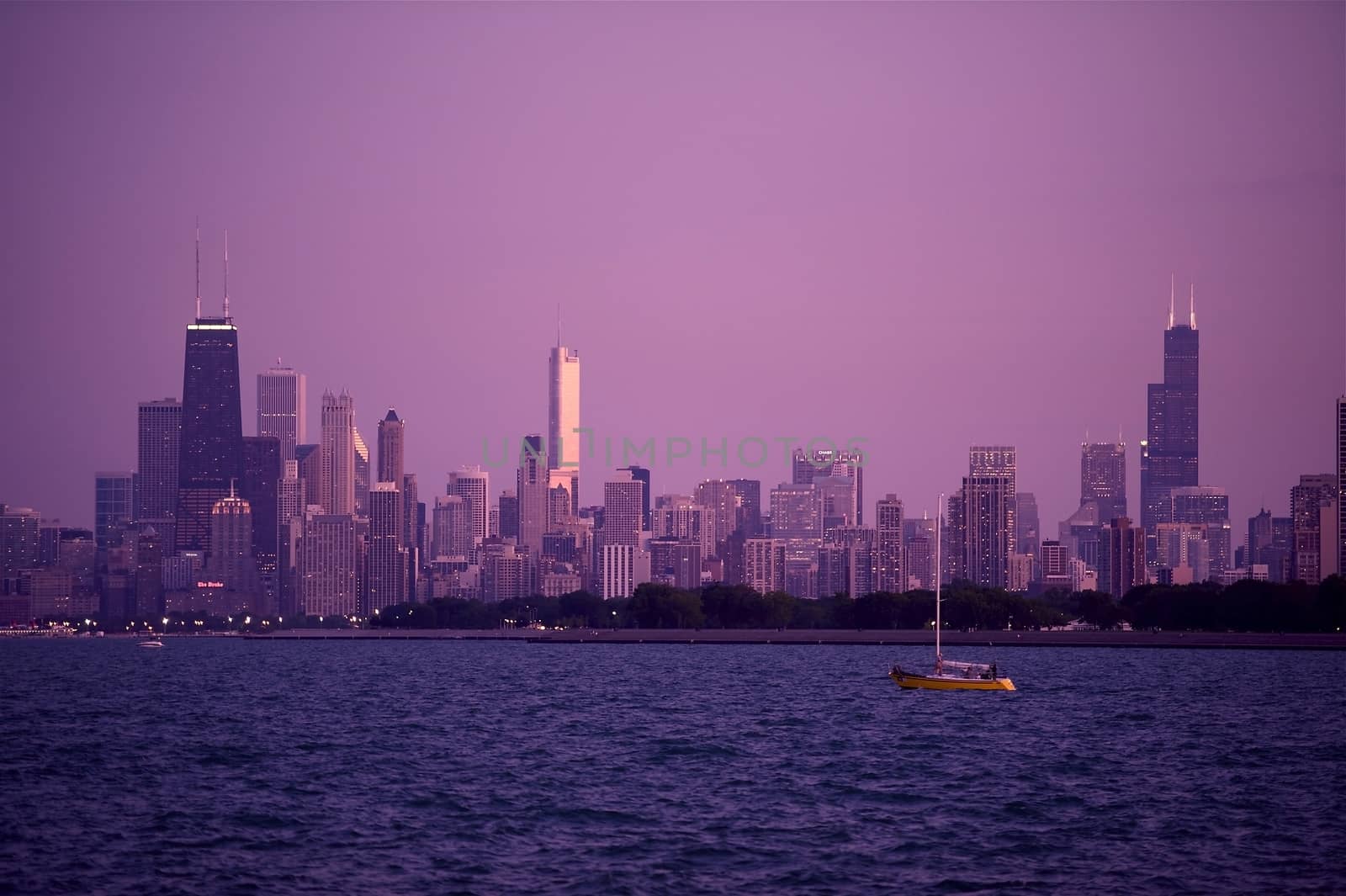 Chicago Skyline Panorama During Sunset. Beautiful Summer Evening in Chicago. Full Chicago Skyline with Small Boat on the Lake Michigan. Hancock Tower on the Left, Trump Tower in the Middle and Sears Tower on the Right Side of the Skyline.