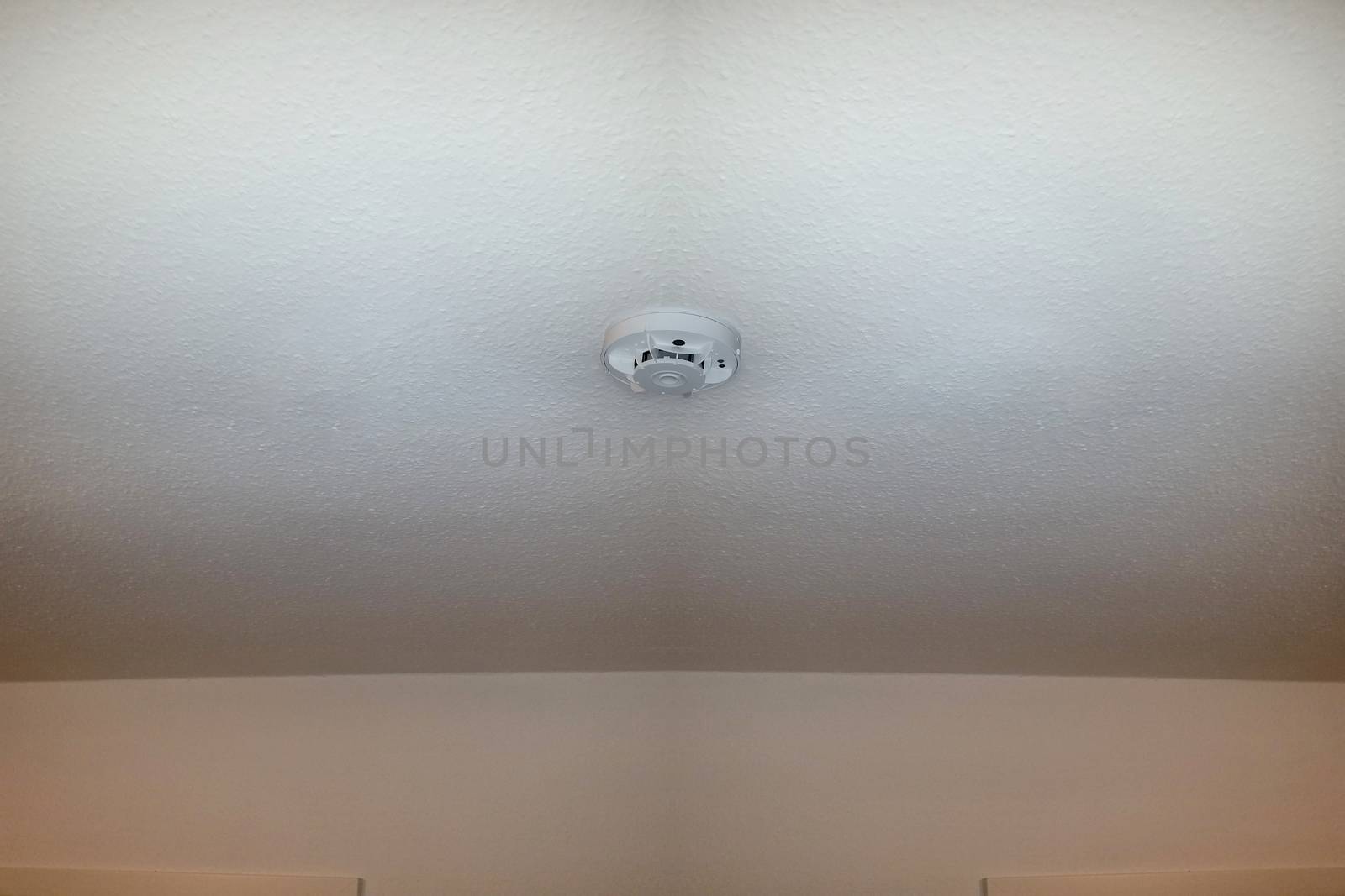 Smoke detector on the ceiling with red warning light sensor and smoke.