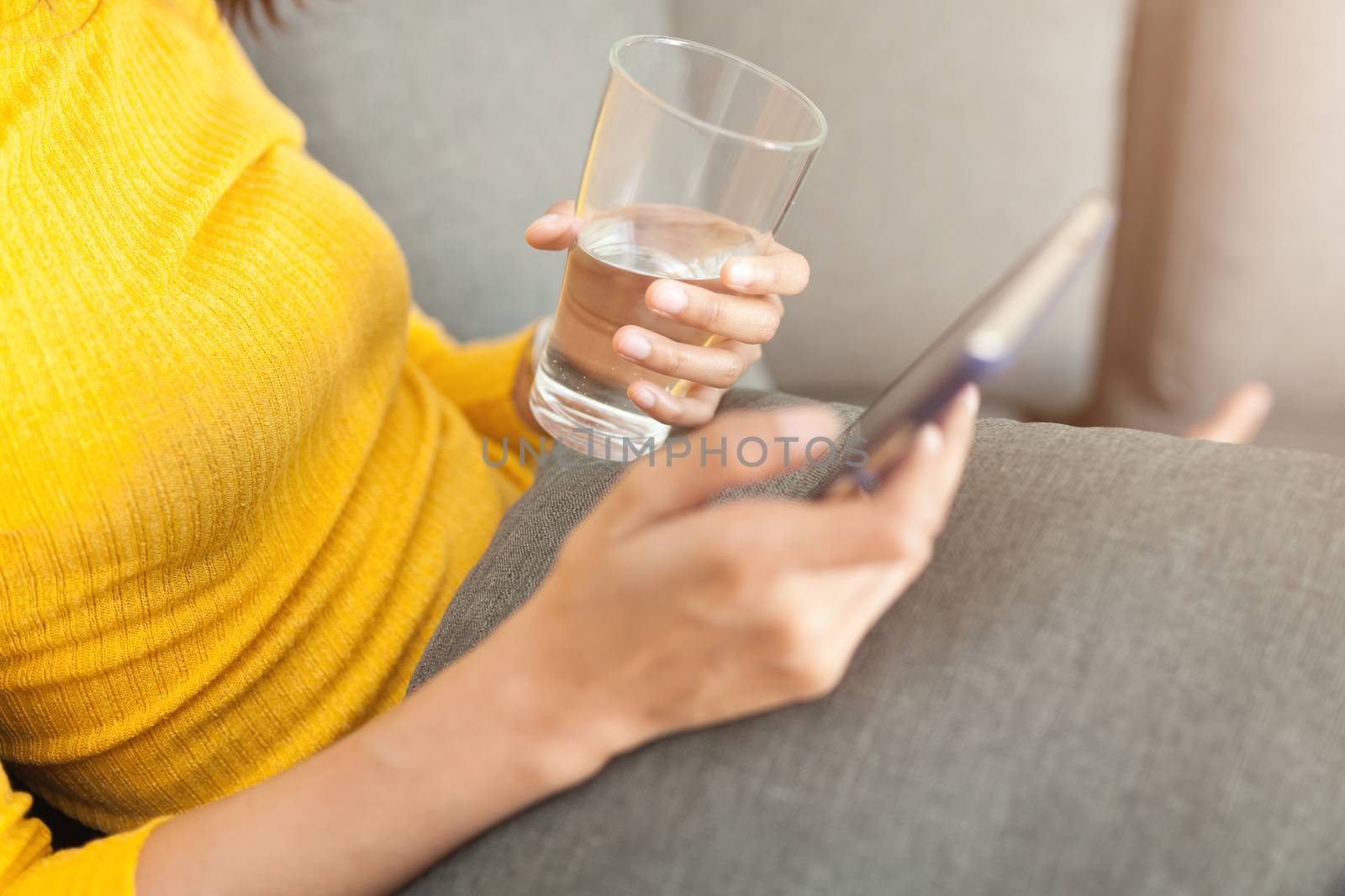 Beautiful woman holding a glass of water and using smartphone by nopparats