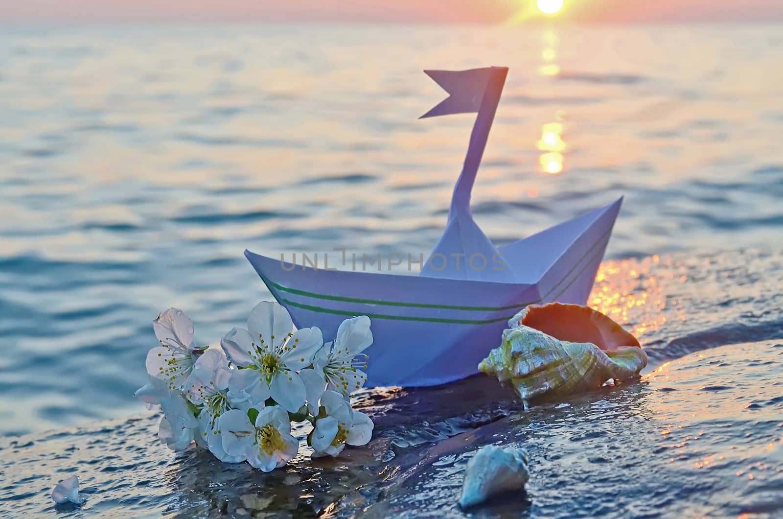 Paper boat, seashells and a sprig of cherry blossoms on a large stone on the seashore