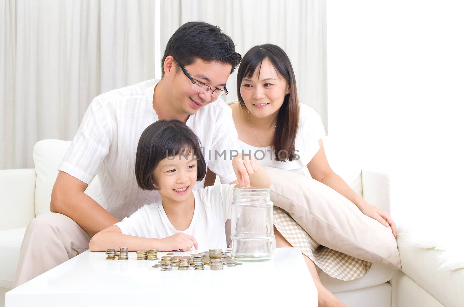 Asian kid putting coins into the glass bottle