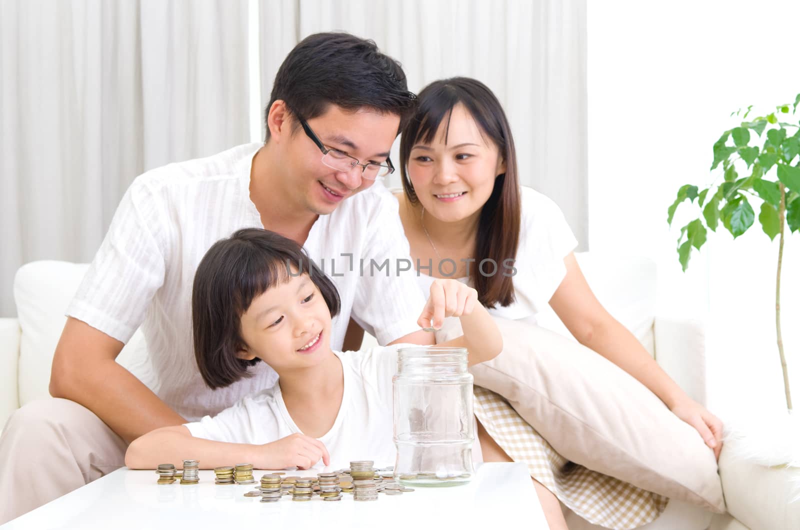 Asian kid putting coins into the glass bottle