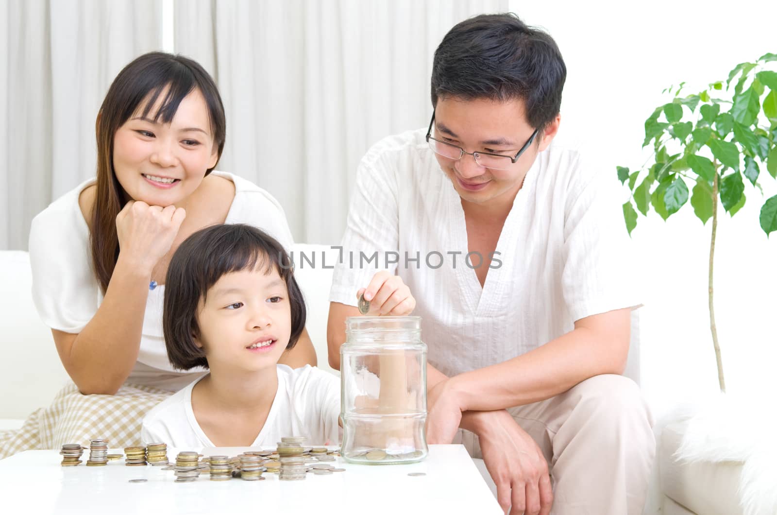 Asian mother and her kid putting coins together into the glass bottle