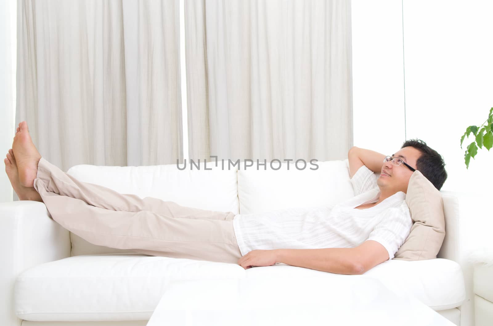 Guy resting and daydreaming at home. Asian handsome man relaxed and lying on sofa indoor.