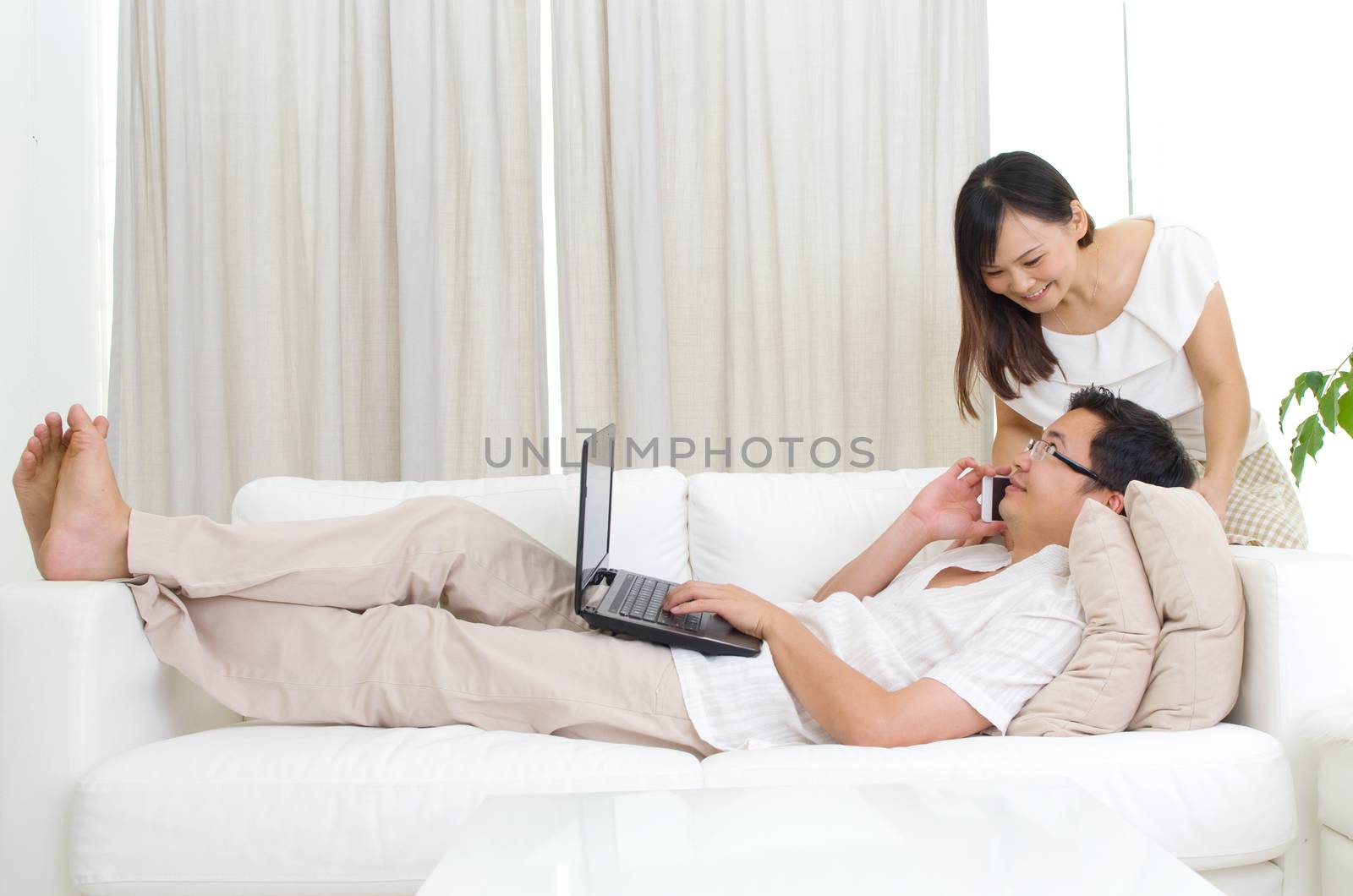 Internet banking apps concept. Husband and wife using smart phone and laptop to perform internet banking. Asian family relaxed at home.