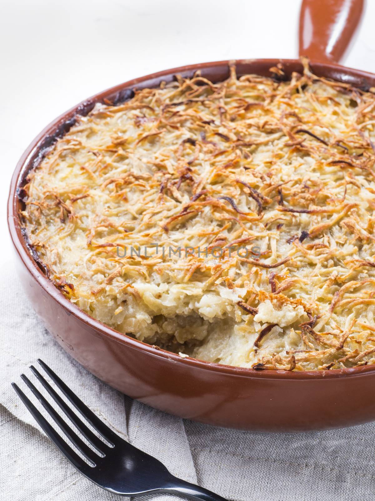 Close up view of appetizing potato casserole with fish, eggs and cream. Potato casserole in serving baking pan on white concrete background
