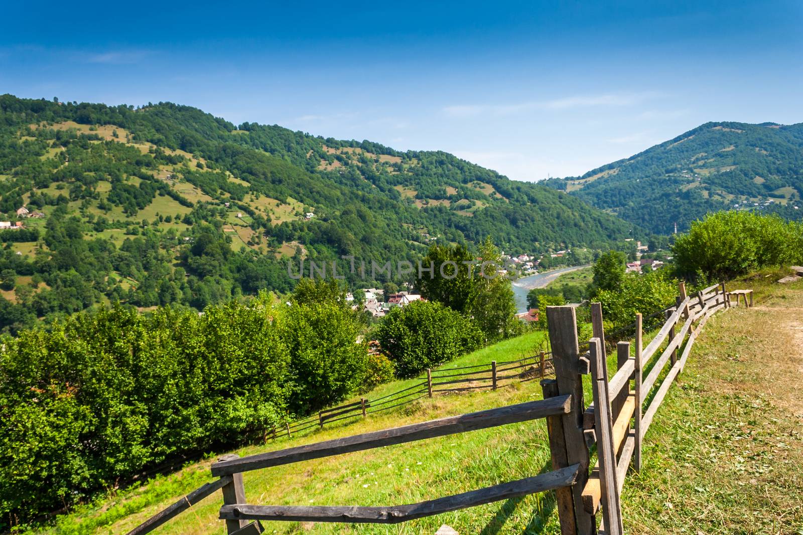 wooden stick fence in vilage in mountains with blue sky, green grass and path in good weather time