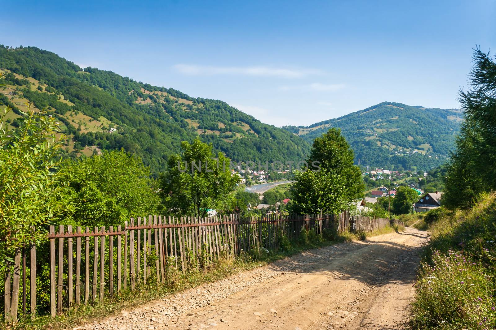 wooden stick fence in vilage in mountains with blue sky, green grass and path in good weather time