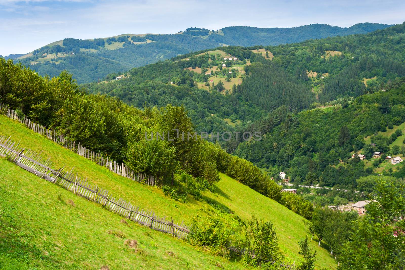 wooden stick fence in village in mountains with blue sky, green grass and path in good weather time