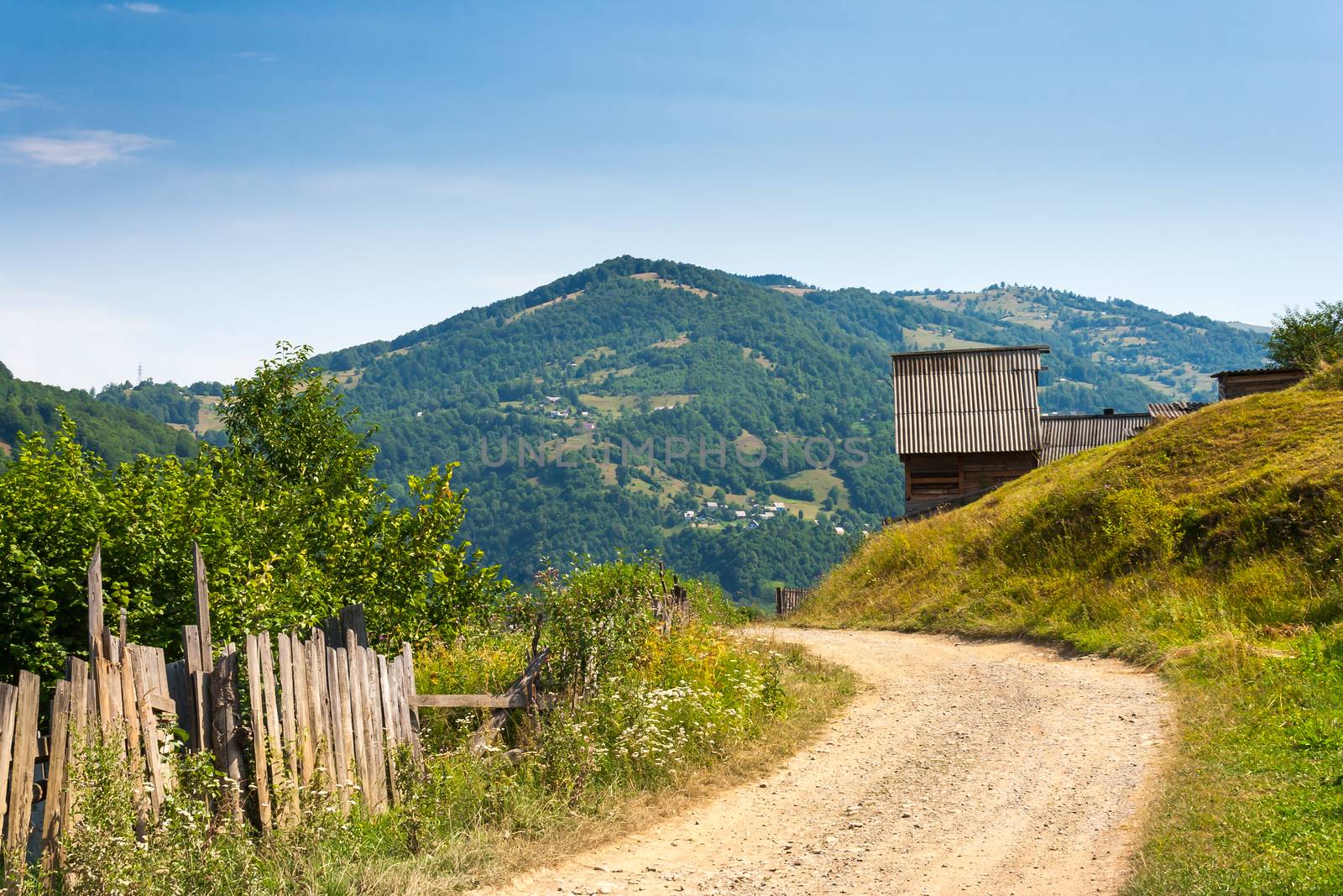 wooden stick fence in village in mountains with blue sky, green grass and path in good weather time