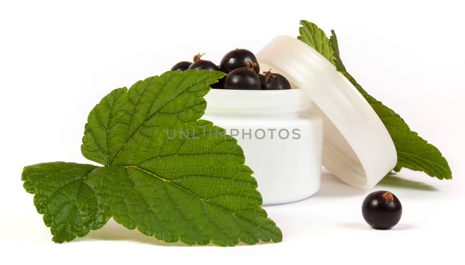 black currants in a jar of makeup with green leaves