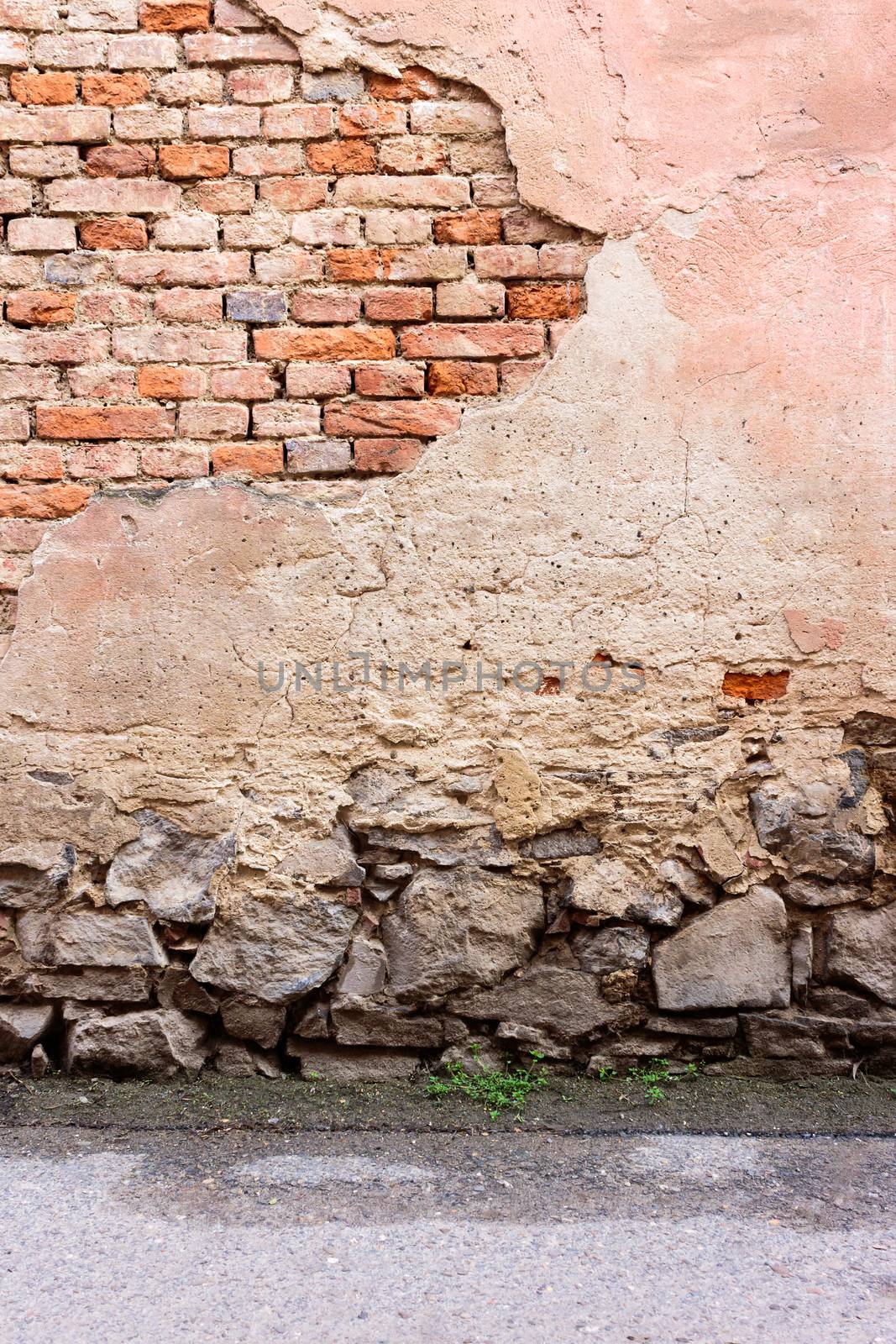 brick wall with chipped plaster, stone foundation and asphalt road