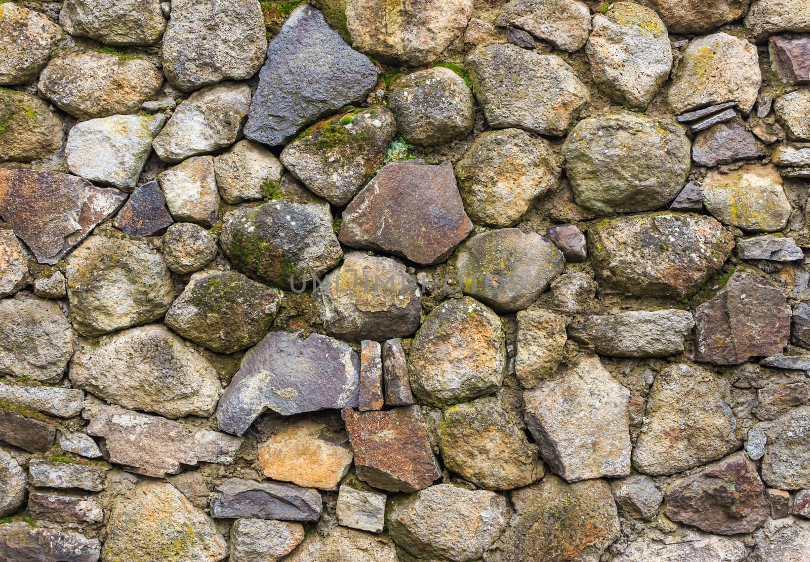 wall of large round and crushed colored stone covered with moss and clay