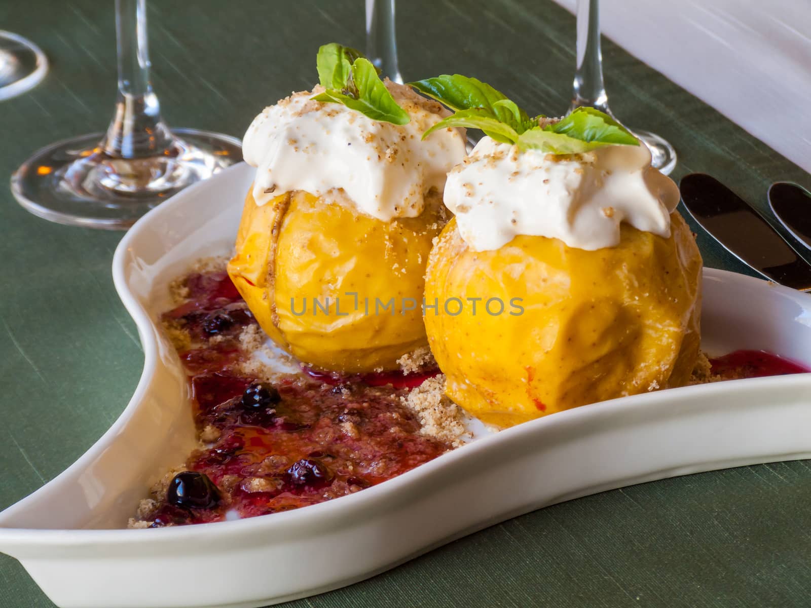yellow and juicy baked apples with jam, decorated with sour cream and chopped nuts, and mint leaves in a triangular plate
