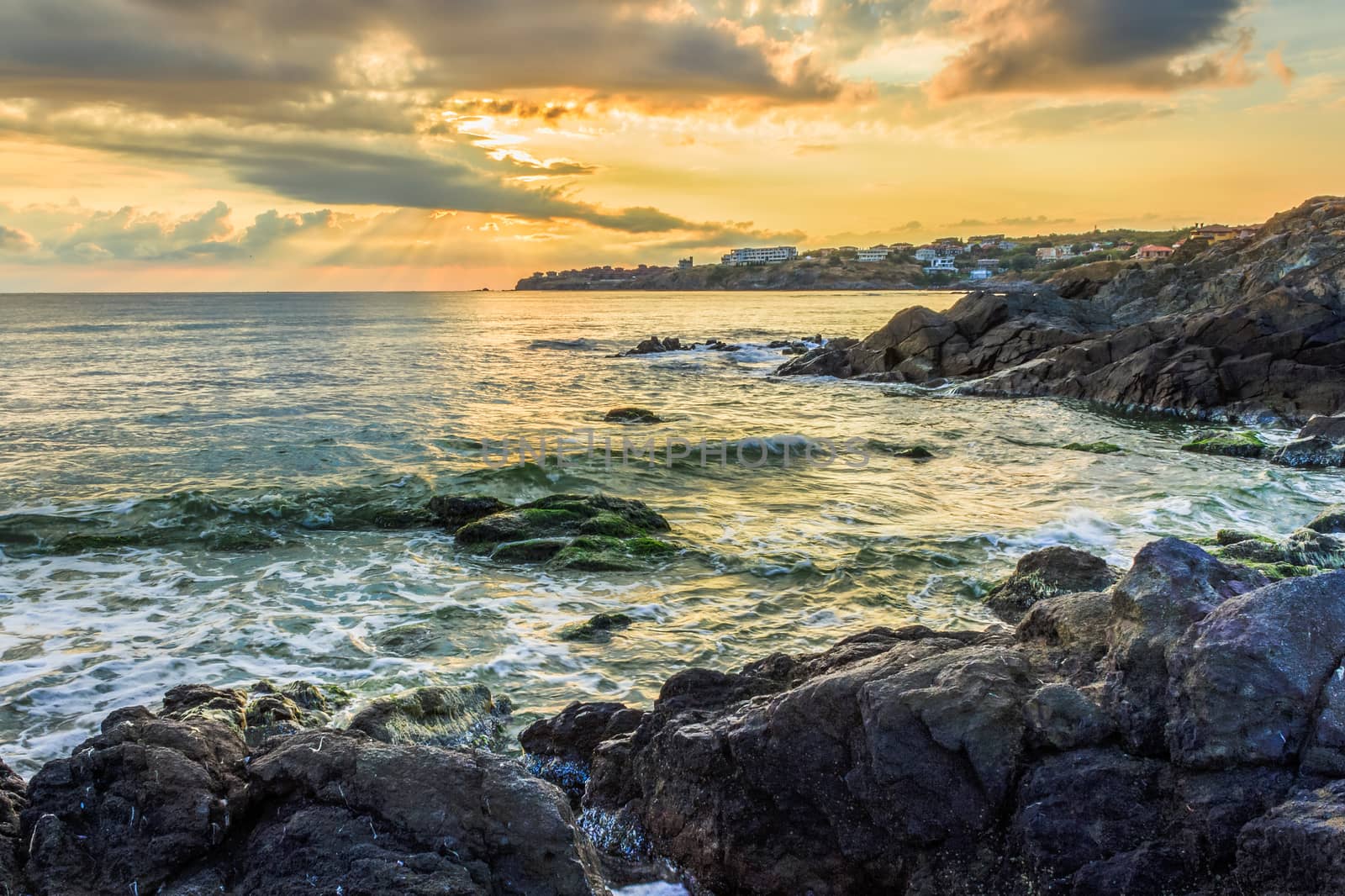 sunrise on the beach, near the small resort village on the edge of the earth. waves breaking on a rocky shore in the sunshine.