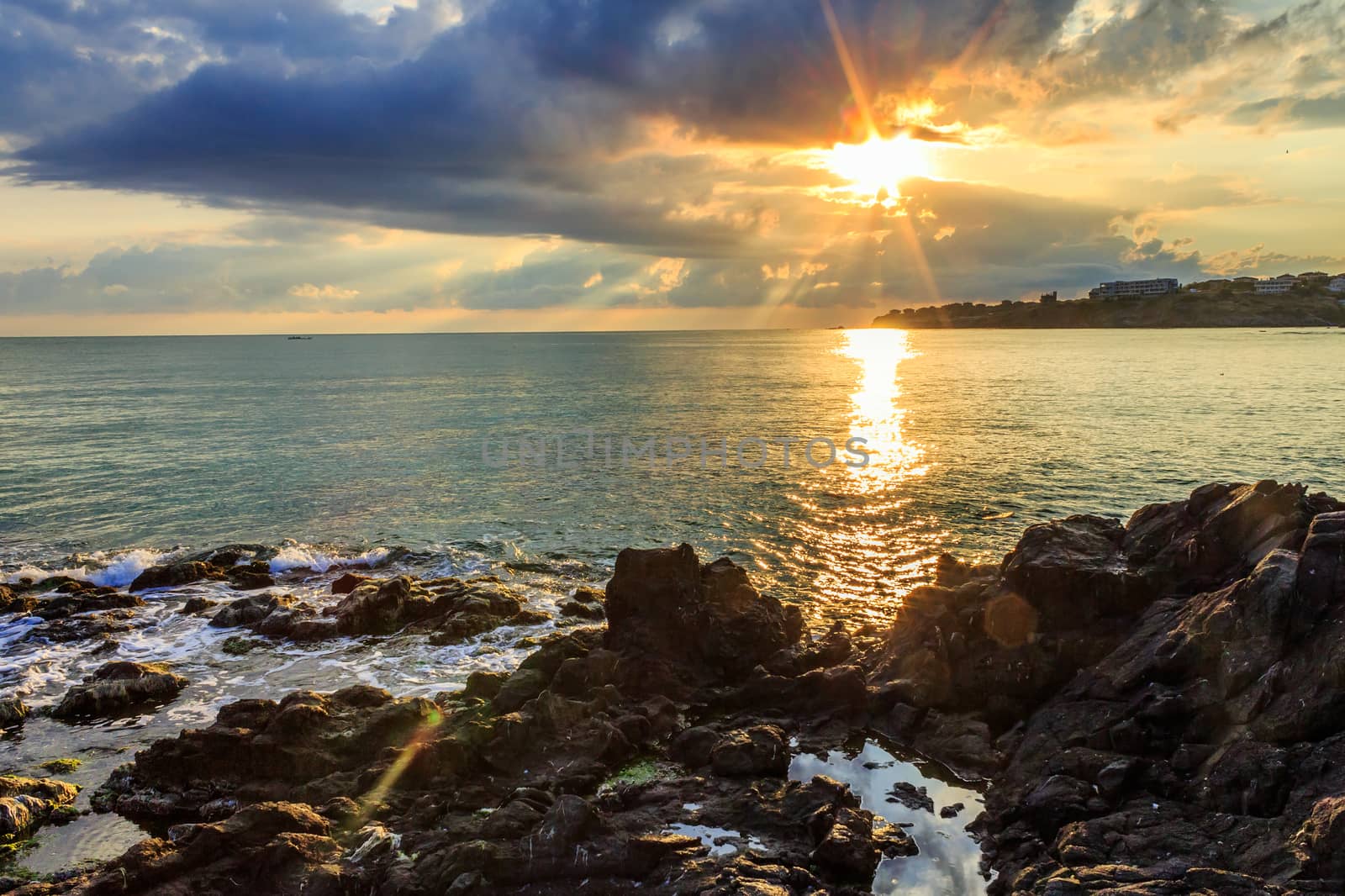 Morning sea landscape with rocky coast, menacing skies, reflections and the rays of the rising sun